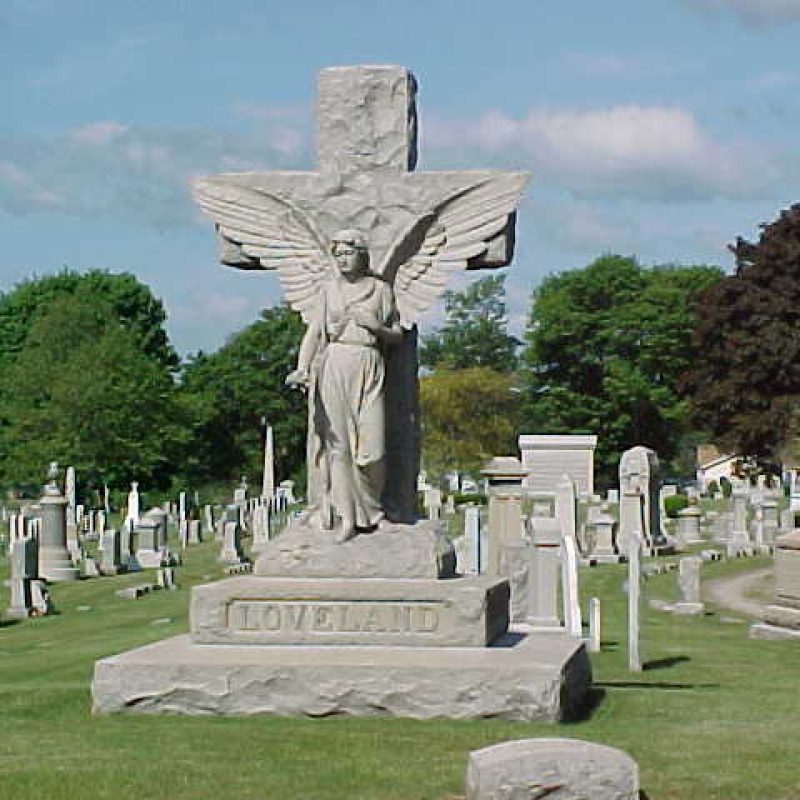 A white monument with a figure on top in a park setting.